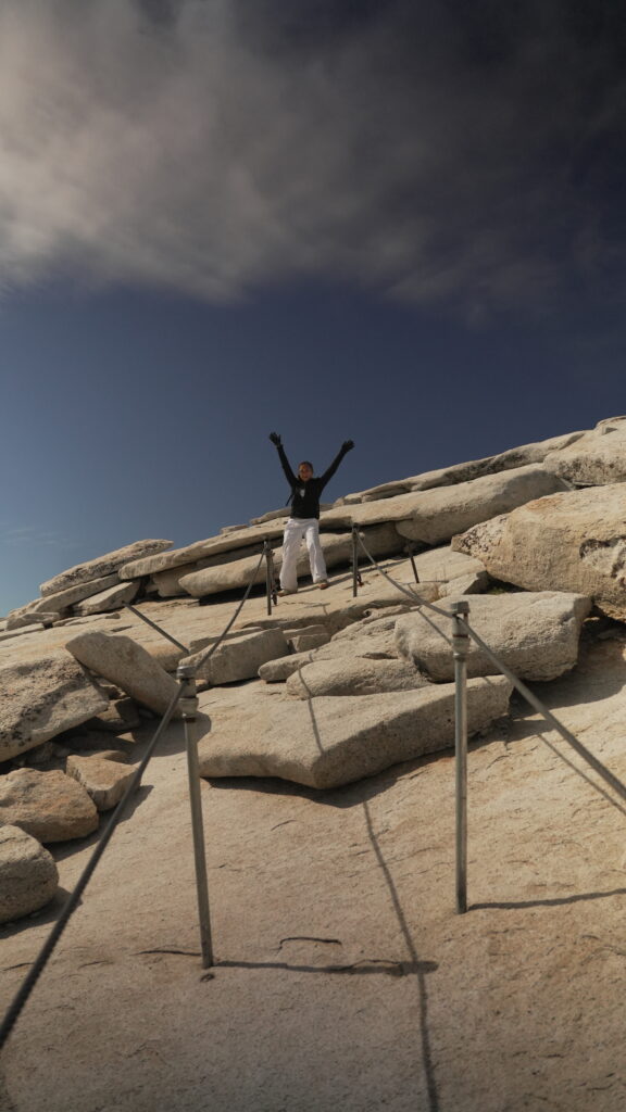 A woman celebrating at the top of the cables at Half Dome