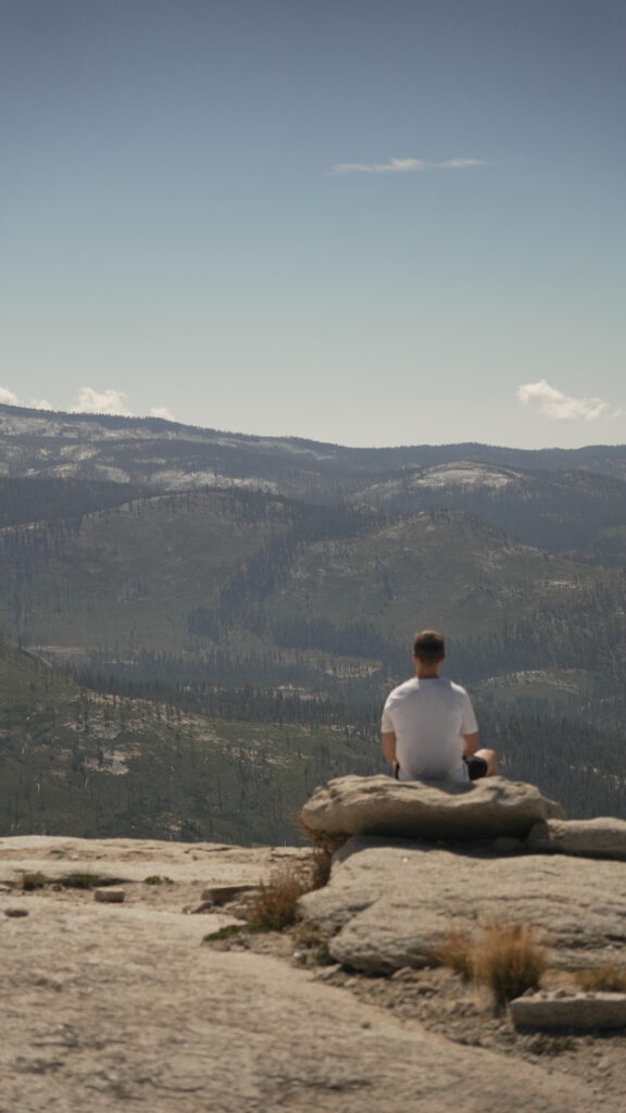 A lone figure sits atop Half Dome